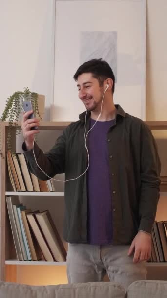 垂直录像 网络电话 细胞连接 远程通信 快乐的男人带着耳机在网上聊天 在舒适的客厅里聊天 — 图库视频影像