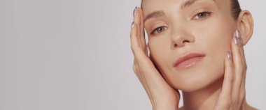 Cilt nemlendirici. Yüz bakımı. Güzellik sağlığı. Çıplak makyajlı bir kadın bej arka planda izole edilmiş yumuşak ve parlak bir yüze dokunmaktan zevk alıyor..