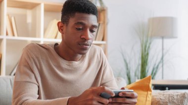 Gadget bağımlılığı. Hücre eğlencesi. Akıllı telefon oyunu. Stresli genç adam evdeki koltukta seyyar esport yarışması izliyor..