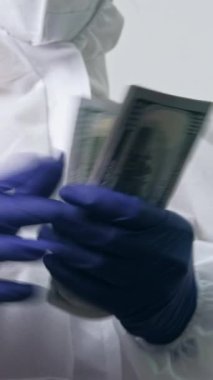 Dikey video. Tıbbi yozlaşma. Doktor rüşveti. Sağlık hizmetleri geliri. Koruyucu giysi uzmanı. Ellerindeki paraları sayıyor..