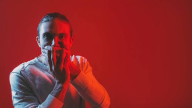 Sessiz ol. Sessizlik uyarısı. Komplo sırrı. Kırmızı renk neon ışık rahatsız erkek elleri karanlık boşluk arka planında ağzını kapatıyor.