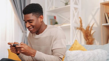 Hücre oyunları. Telefon eğlencesi. Dijital bir eğlence. Evdeki oturma odasındaki koltukta özel muamele uygulaması çalan mutlu genç adam..