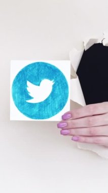 Kharkiv, Ukrayna - Haziran 04, 2020: Dikey video. Twitter simgesi. Sosyal medya. Beyaz boş arkaplan üzerinde uygulama logosu gösteren bir kağıt deliğinin içindeki kadın blog yazarı eli.