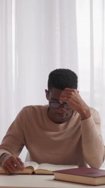 Dikey video. Yorgun öğrenci. Basınç öğreniyorum. Yorgun ve uykulu genç adam kitap ödevi araştırıyor ev masasında üniversite sınavlarına hazırlanıyor..