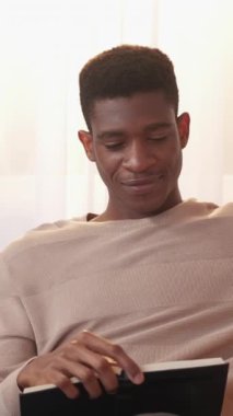 Dikey video. Roman okuyorum. Edebiyat hobisi. Ev tatili. Keyifli ve rahat genç adam ilginç kağıt çok satanlar kitabında dinleniyor..