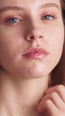 Dikey video. Mükemmel cilt. Yüzün iyi olsun. Kadın kozmetiği. Güzellik bakımı. Kendine güveni olmayan, doğal makyajlı, çıplak göz farı ve ruju olan genç bir kadın..