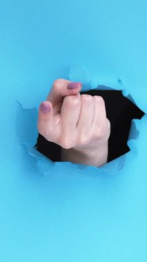 Dikey video. - Gel buraya. Jesti izle. Mavi yırtık kağıt duvar üzerinde parmak deliğiyle davet kadın el boş alan ile reklam arka planı.