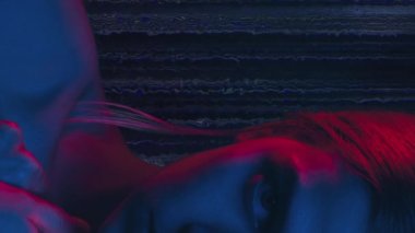 Dikey video. Kadın hakları için. Cinsiyet ayrımcılığı. Öfkeli kadın, koyu renk hareketli arka planda kırmızı mavi ışıklı portre içinde yarı suratlı..