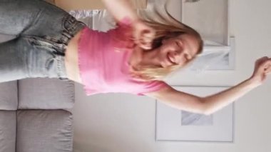 Dikey video. Sabah eğlencesi. Ev eğlencesi. Enerji aktivitesi. Mutlu, güler yüzlü, dans eden, zıplayan, aydınlık iç odada yeni günün tadını çıkaran kadın..