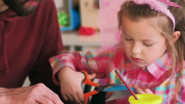 手工制作的儿童礼物 父亲的帮助快乐的父亲支持着充满热情的女儿 小女孩的业余爱好就是在桌旁剪彩纸 — 图库视频影像
