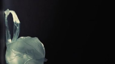 Dikey video. Plastik kirliliği. Atık yönetimi. Kirliliği durdurun. Kullanılmış selofan poşetler çöp yığınına düşüyor. Karanlık arka plan boşluğuna izole edilmiş..