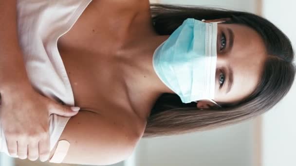 垂直ビデオ 感染予防 健康保護 病気が広がる 若いです幸せな笑顔穏やかな女性とともにパッチオン腕で医療面マスクでライトインテリア — ストック動画