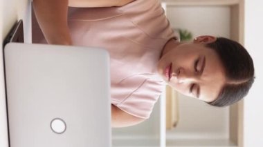 Dikey video. Stresli bir iş. Bilgisayar boyunlu. Ofis esnemesi. Konsantrasyon sorunları. Somurtkan iş kadını laptopun başına oturmuş, iç kısımda ısınıyor..