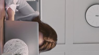 Dikey video. Ofis keyfi. İş sorumsuzluğu. Tembel kadın sekreter iş yerinde patron dışarıda otururken cep telefonu kullanıyormuş gibi yapıyor..