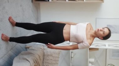 Dikey video. Yorucu bir egzersiz. Spor yorgunluğu. Kadın antrenmanı, dizleri titrek, sırtüstü uzanmış, koltuğa uzanmış, evinde dinleniyor..