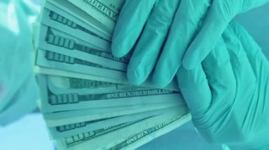Dikey video. Sağlık sigortası masrafları. Tıbbi yozlaşma. Doktor maaşı. Cerrah koruyucu ekipman içinde Amerikan doları nakit para fanı tutuyor..