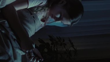 Dikey video. Çocuk takıntısı. Gece gezmesi. Kaydırma. Uykulu esneyen kız internette akıllı telefondan gülüyor karanlık odada..