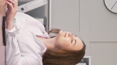 Dikey video. Ofis sakin. Tembellik. Memnun iş kadını iş yerinde dinleniyor, iş yerinde oturuyor..