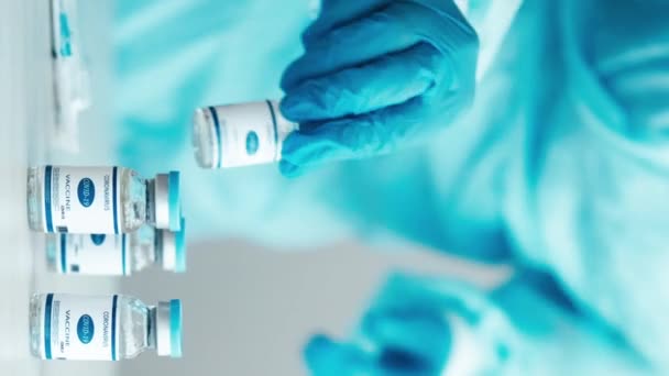 垂直ビデオ コロナウイルスワクチン 筋肉内注射 テーブルの上の薬瓶 看護師で青い制服と手袋で注射器と女性患者でマスクでクリニック — ストック動画