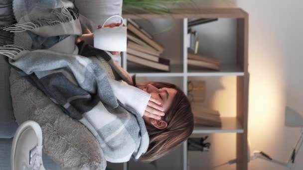 垂直录像 生病的茶 病毒饮用 喉咙闷死了发抖的女人感冒了 手握治疗杯 坐在沙发上 裹着毛毯 躺在家里 — 图库视频影像