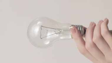 Dikey video. Ampul. Yaratıcı bir fikir. Gri boş arkaplanda izole edilmiş elektrikli araç akıllı çözelti gösteren kadın el.