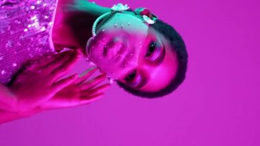 Dikey video. Pandemik moda. Karantina aksesuarı. Şenlikli güzellik. Mor pembe neon ışıklı cazibeli kadın. Ağlı maske takıyor. Parlak pullu elbise..