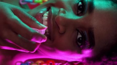 Dikey video. Dudak nemlendirici. Parti makyajı. Cilt bakım ürünleri. Kendine güvenen, güler yüzlü, parlak yüzlü bir kadın. Renkli, neon ışıkla parlatıcı sürüyor..