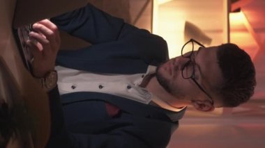 Dikey video. Online eğitim. Erkek öğretmen. Ders hazırlığı. Masanın üzerinde karanlık odanın içinde açık kitaplarla dizüstü bilgisayarı yazan konsantre bir adam..