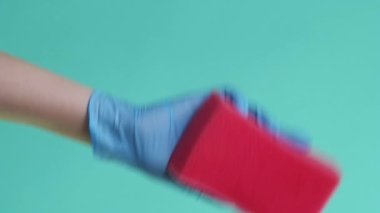 Dikey video. Ev aletleri. Yüzey temizliği. Profesyonel hademe, lateks eldiven giymiş. Temizlik yaparken yeşil arka planda kırmızı sünger var..