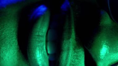 Dikey video. Neon gülüşü. Diş beyazlatma. Diş bakımı. Yeşil renkli ışık, tanımlanamayan neşeli, mutlu adamın koyu mavi yüzlü yüzü..