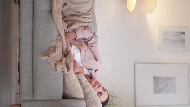 垂直录像 发烧关心 流感症状 小心翼翼的少女把一杯水带给躺在光线室室内沙发上的生病妇女 — 图库视频影像