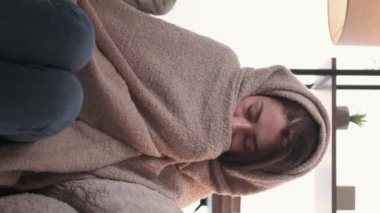 Dikey video. Enfeksiyon kapmış. Hasta kadın. Evde iyileşme. Acı çeken kadın, kareli kanepeye sarılı, hapşıran peçete, kendini kötü hissediyor..