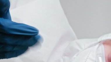 Dikey video. Laboratuvar teknisyeni. Coronavirus aşısı. Beyaz elbiseli hemşire eldiven takıp hastayı tıbbi prosedüre davet ediyor..