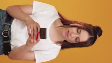 Dikey video. Gezici sohbet. Kısa mesaj. Turuncu arka planda modern akıllı telefon sosyal medya uygulaması yazan mutlu bir kadın..