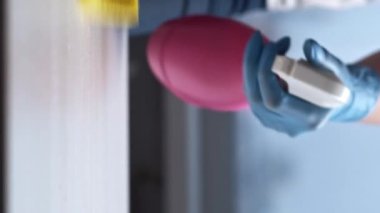 Dikey video. Profesyonel deterjan. Mobilya temizliği. Hademe eldivenlerini giyip, evdeki sarı süngerle şişe temizleyicisinden sprey sıkar..