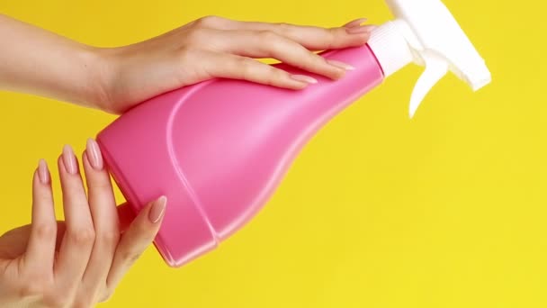バーティカルビデオ 広告クリーニング製品 ホームチェア 黄色い背景に隔離された手の洗剤の液体が付いているピンクの世帯用用具のスプレー ボトルが付いている女性 — ストック動画