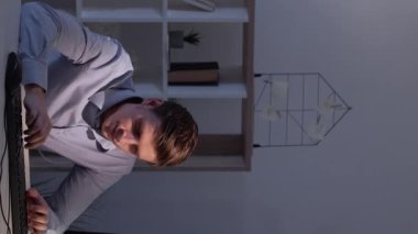Dikey video. Bir sürü iş. Yorgun adam. Çevrimiçi iletişim. Ofisteki adam klavye ışığı gölge odasını hızlı çekimde yazarken yorgun hissediyor..