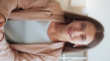 Dikey video. Çevrimiçi iletişim. İçten bir sevinç. Terapi desteği. Duygusal olarak şaşırmış, iş elbisesi içinde gülümseyen, el kol hareketi yapan, içten içe duygularını ifade eden bir kadın..