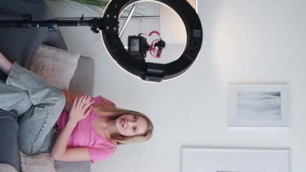 垂直ビデオ 女性のVlog ブロガーのアドバイスだ 陽気な感情的な若い女性の記録内容は 自宅でリングランプと白い部屋で三脚の上にカメラに話して — ストック動画