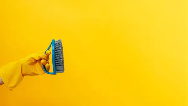 Cleaning tools. Washing equipment. Home hygiene. Professional janitor hand in protective gloves with brush isolated on yellow background empty space.