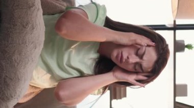 Dikey video. Baş ağrısı çekiyor. Hasta kadın. Ev hastalığı. Yorgun bir kadın kafasında dayanılmaz bir acı hissediyor. Mesajlaşmalar, tapınaklar, aydınlık odanın içinde oturuyor..