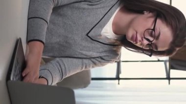 Dikey video. Sıkı eğitim. Gergin kadın. Online iş. Sıradan bir bayan dizüstü bilgisayarı kapatıyor. Boyun masajı yapıyor. Masa lambasının iç tarafındaki görevleri tamamlıyor..