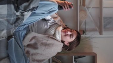 Dikey video. İnternetten hasta numarası. İnternet konuşması. Ekoseye sarılı sağlıksız bir kız telefonda konuşuyor..