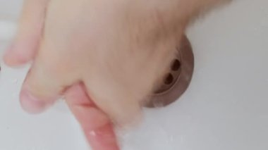 Dikey video. Hijyen alışkanlığı. El yıkama. Avuçlarını suyun altında ovuşturan adam beyaz lavaboda yayılan bakteri virüsünden deriyi düzgün koruyor..