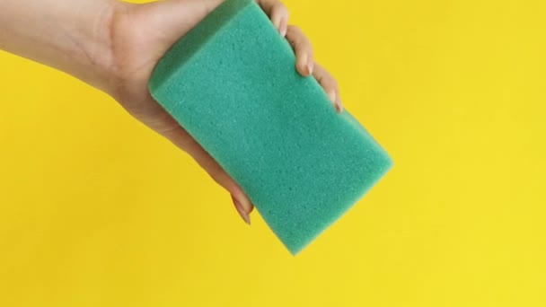 バーティカルビデオ ハウス チェアス 国内クリーニング ジャニスターサービス 黄色い背景のコピースペースで隔離された緑色のピンクの洗浄スポンジを絞る女性の手 — ストック動画