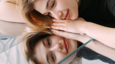 Gülen surat. Ayna yansıması. Mutlu, sakin, çekici kadın itici yüzeyde uzanıyor. Hoş düşünceler hayal ediyor..