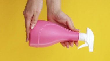Dikey video. Deterjan sıvısı. Daha temiz reklamlar. Hijyen aletleri. Sarı arka planda izole edilmiş antibakteriyel sprey şişesi gösteren kadın eli..