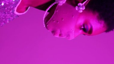 Dikey video. Yüz aksesuarı. Karantina modası. Salgın partisi. Mor pembe, neon ışıklı, kendine güvenen, boş arkaplanda maske takan bir kadın profili..