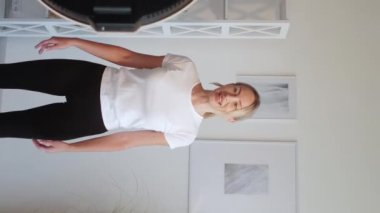 Dikey video. Çevrimiçi ev sporu. Fitness kaydı. Gülümseyen kadın egzersiz yapıyor. Egzersiz tekniğini anlatıyor. İç mekanda kamera ışığı ekipmanı kullanıyor..