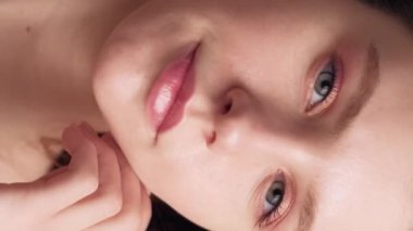 Dikey video. Cilt sağlığı. Güzellik tedavisi. Doğal makyaj. Çıplak göz farı ve ruj sürmüş genç bir kadın. Parlak yüzüne elinle dokunuyor..